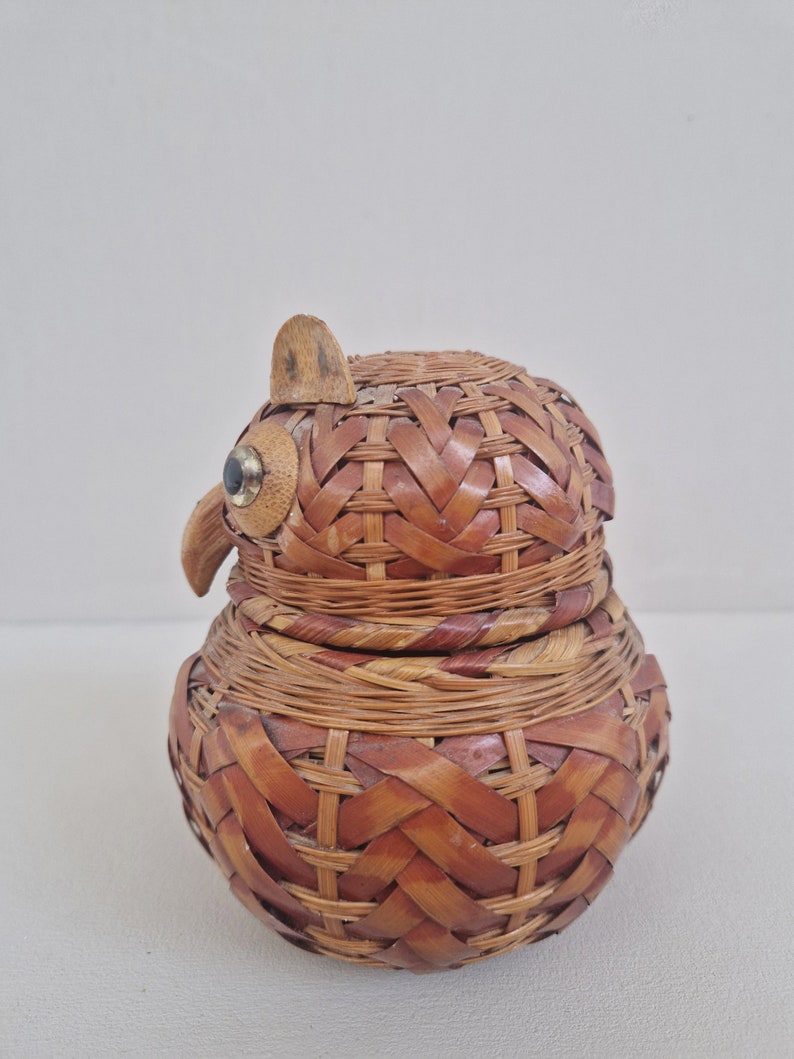 May include: A woven wicker owl-shaped container with a brown and tan color scheme. The owl has a small wooden beak and black eyes.