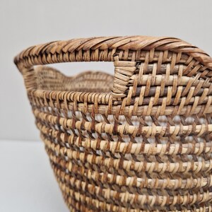 May include: A woven wicker basket with a handle. The basket is made of natural brown and tan colored wicker.