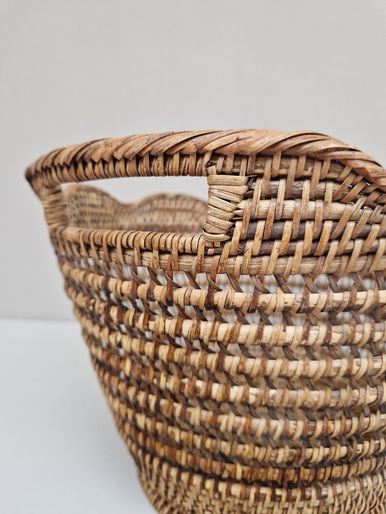 May include: A woven wicker basket with a handle. The basket is made of natural brown and tan colored wicker.
