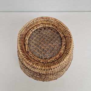 May include: A round, woven wicker basket with a brown and tan color scheme. The basket has a woven lid with a circular opening in the center.