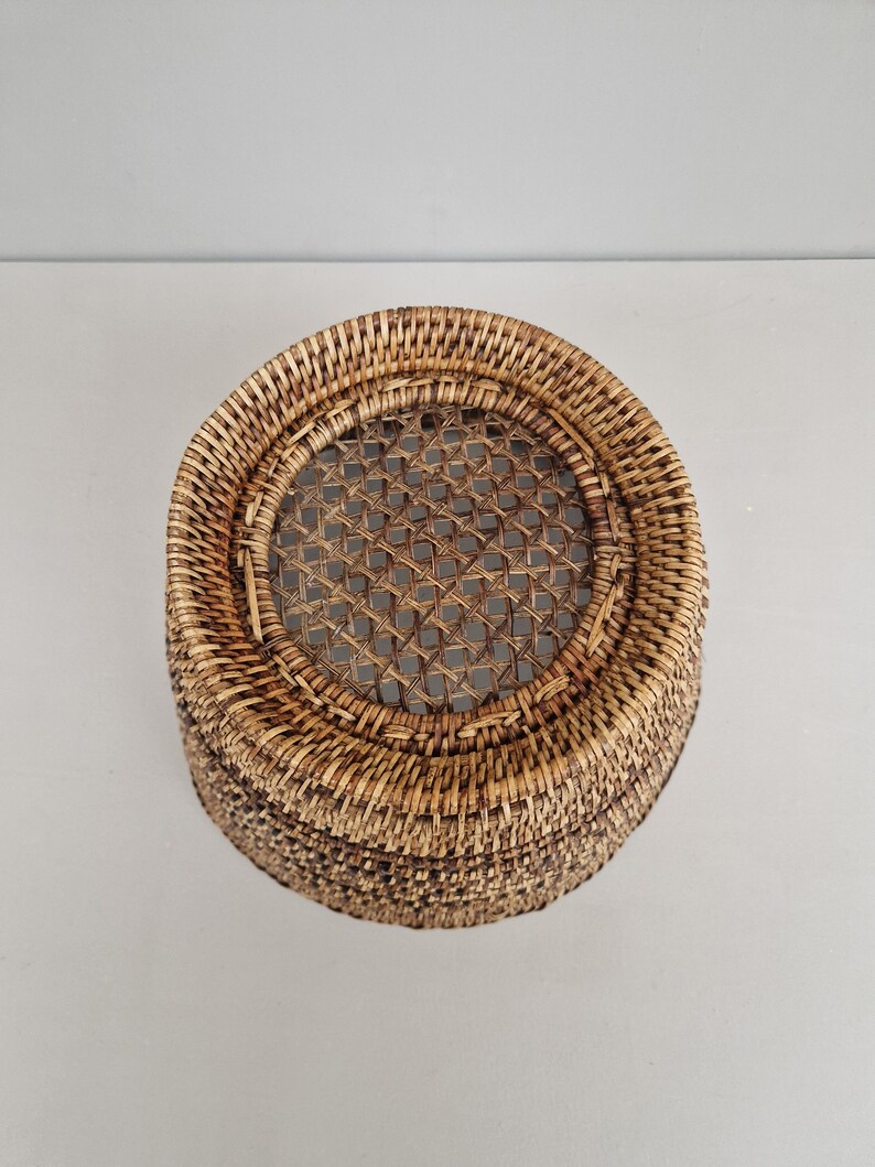 May include: A round, woven wicker basket with a brown and tan color scheme. The basket has a woven lid with a circular opening in the center.