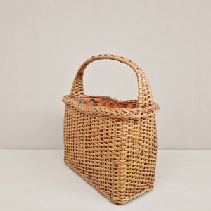 May include: A woven wicker basket with a single handle. The basket is rectangular with a slightly rounded top and a natural brown color.