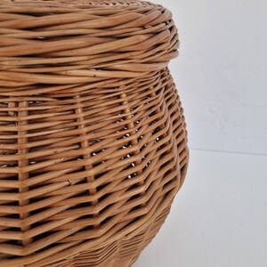 May include: A woven wicker basket with a lid. The basket is light brown and has a rounded shape.