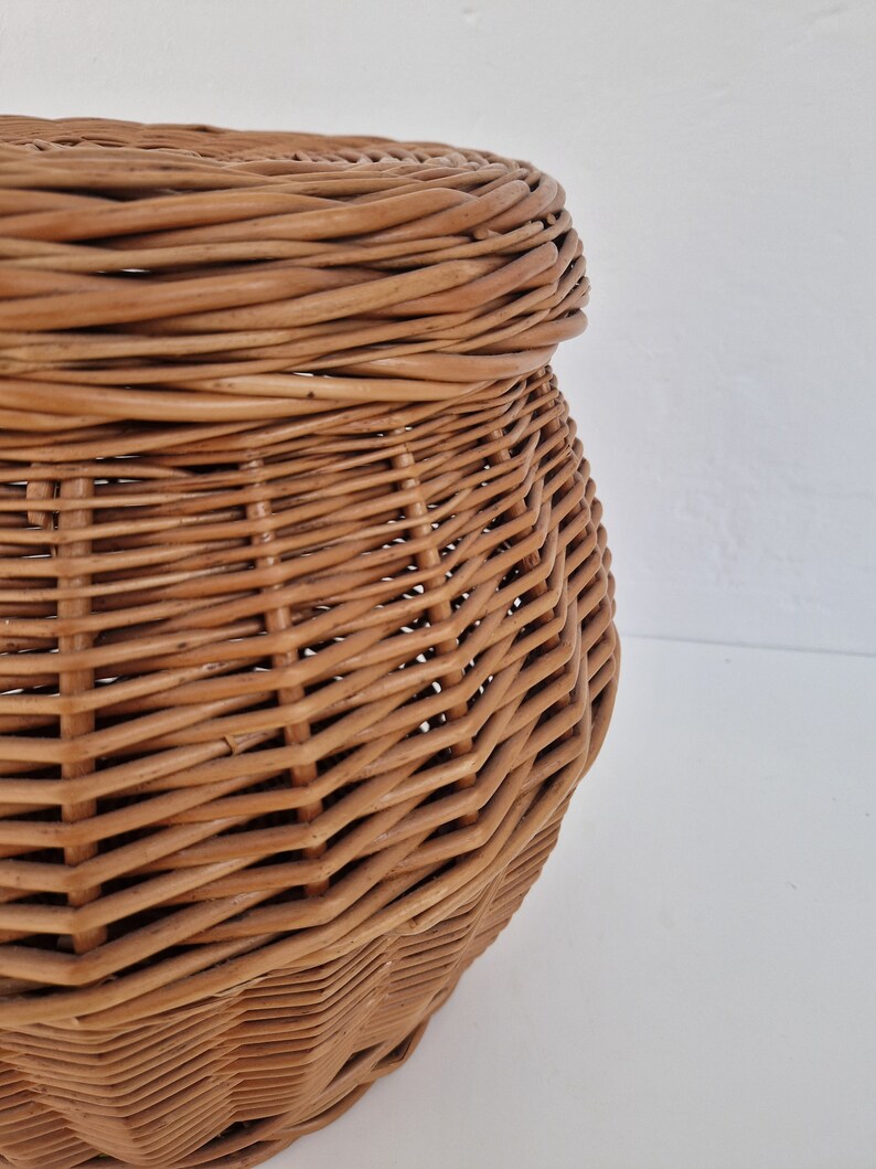 May include: A woven wicker basket with a lid. The basket is light brown and has a rounded shape.