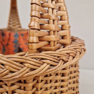 May include: A woven wicker basket with a brown handle. The basket is made of natural materials and has a rustic look.