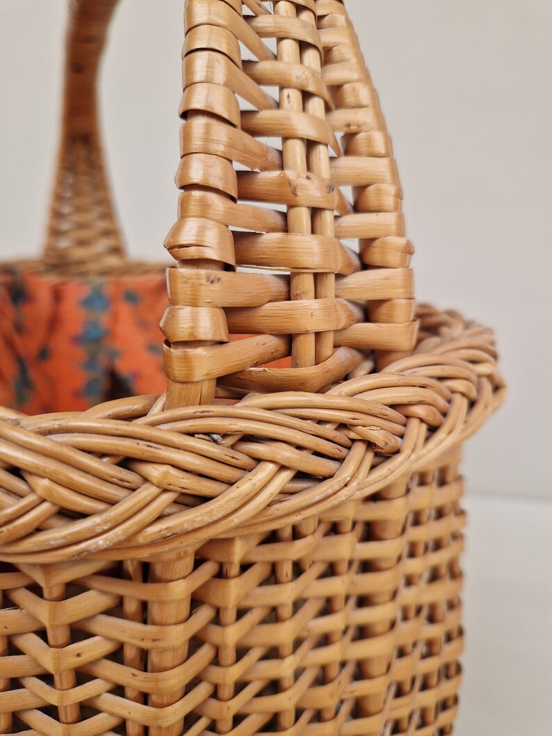 May include: A woven wicker basket with a brown handle. The basket is made of natural materials and has a rustic look.