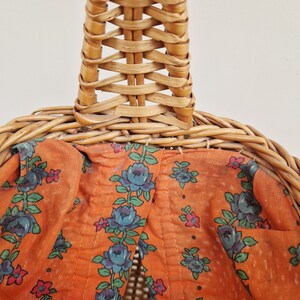 May include: A woven wicker basket with a brown fabric lining featuring a floral pattern of blue flowers and red accents.