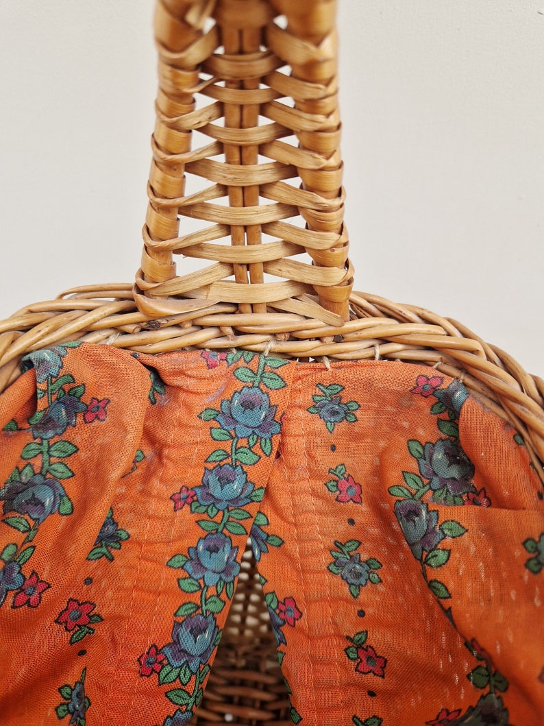 May include: A woven wicker basket with a brown fabric lining featuring a floral pattern of blue flowers and red accents.