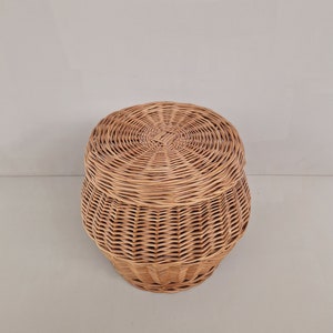May include: A round wicker basket with a lid. The basket is made of natural woven wicker and has a light brown color.