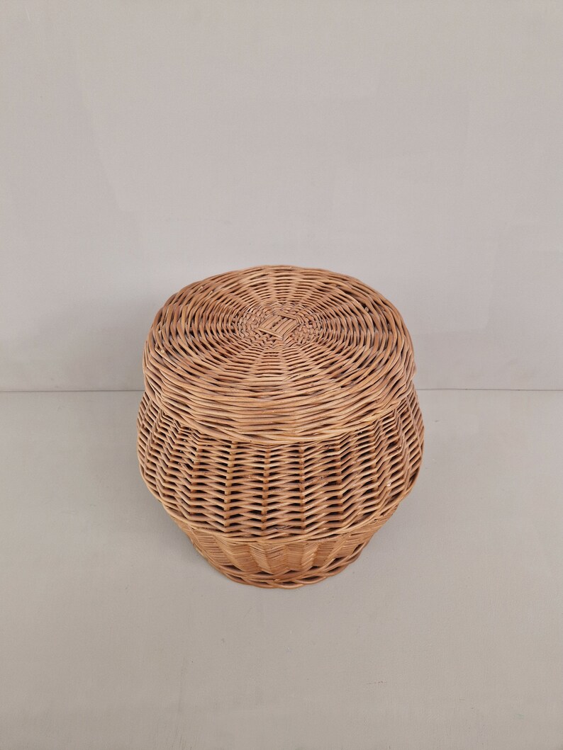 May include: A round wicker basket with a lid. The basket is made of natural woven wicker and has a light brown color.