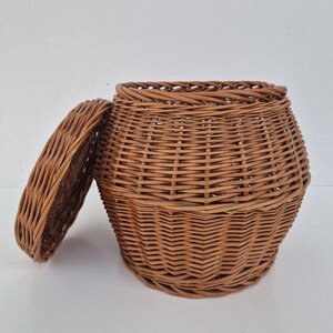 May include: A brown wicker basket with a lid. The basket is woven with a tight pattern and has a rounded shape.