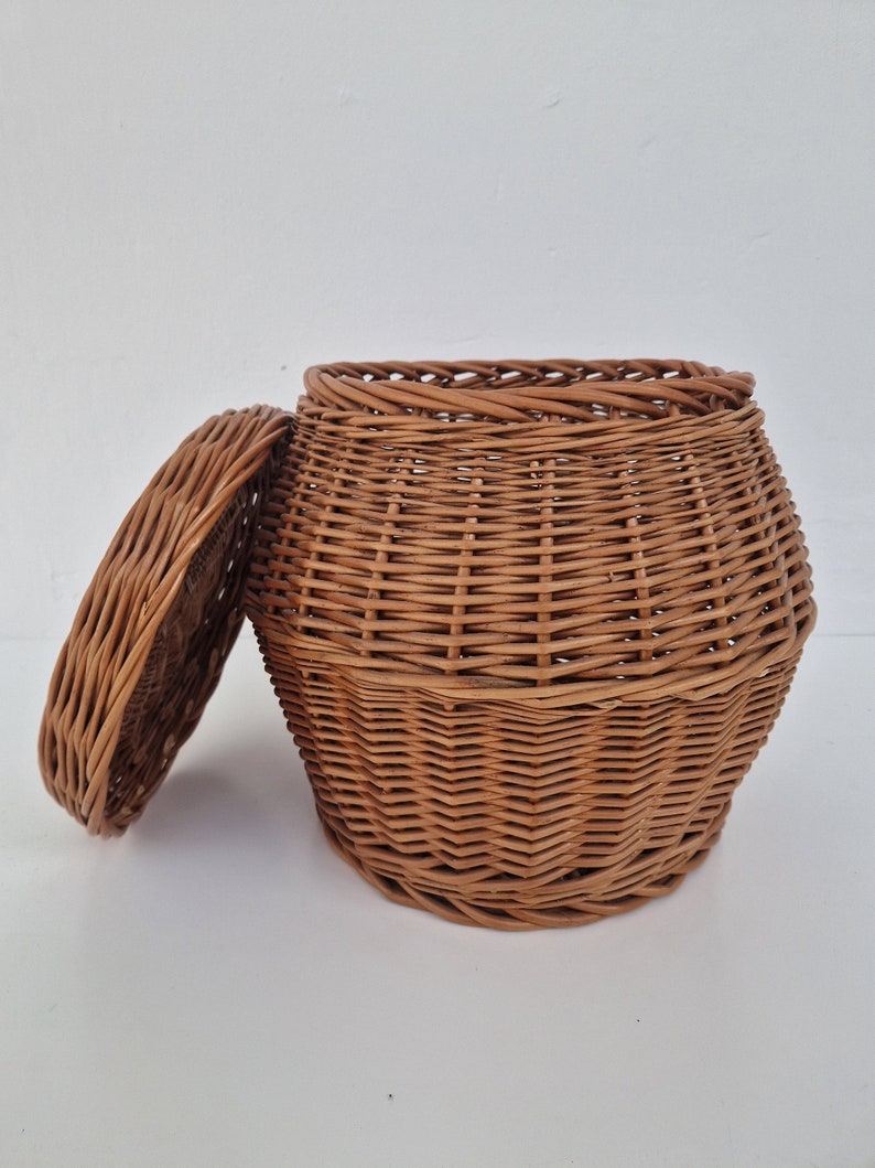 May include: A brown wicker basket with a lid. The basket is woven with a tight pattern and has a rounded shape.