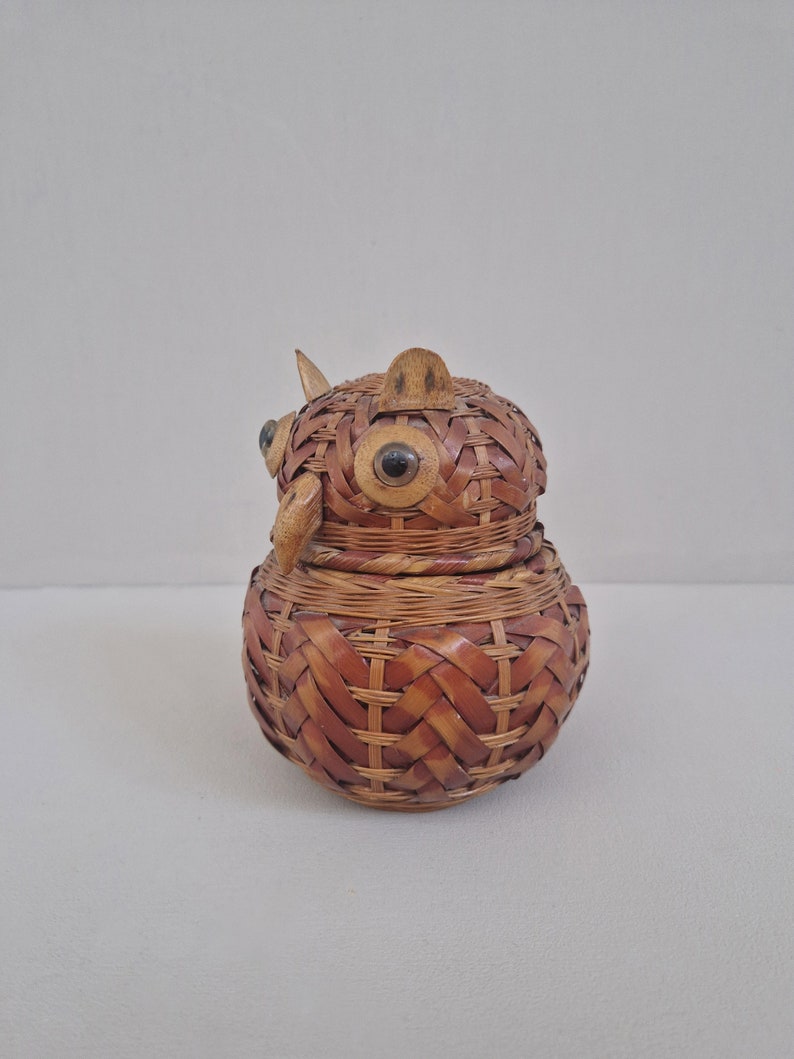 May include: A woven wicker owl-shaped trinket box with black eyes. The box is brown and has a woven pattern.