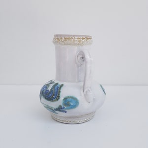 K&ouml;nnte beinhalten: Wei&szlig;e Keramikvase mit blauem und gr&uuml;nem Blumendesign. Die Vase hat einen runden K&ouml;rper und einen kleinen Henkel.