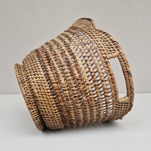 May include: A woven wicker basket with a rounded shape and a handle on the side. The basket is made of natural brown rattan.