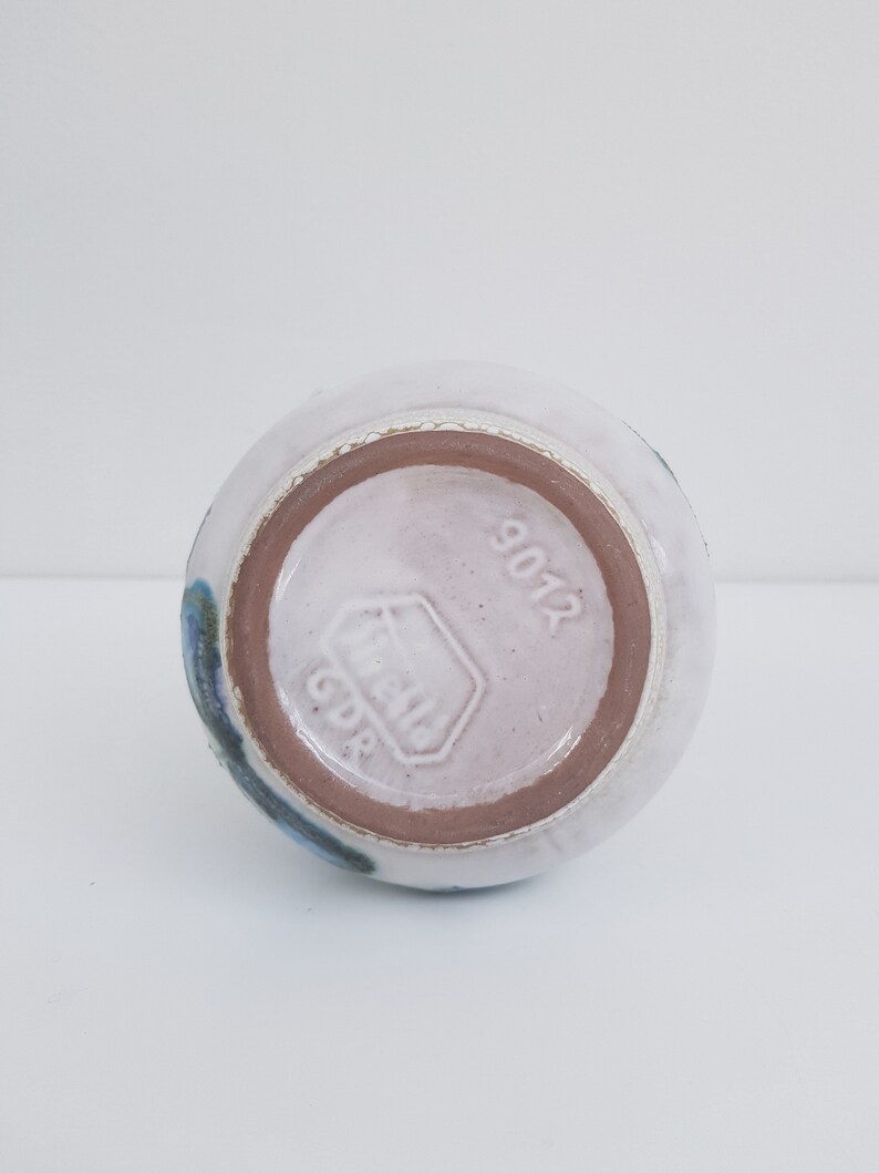 K&ouml;nnte beinhalten: Die Unterseite einer wei&szlig;en Keramikvase mit blauem und braunem &Uuml;berzug. Die Vase ist mit "GDR" und "9012" gestempelt.