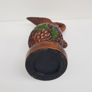 May include: A brown ceramic pitcher with a textured body and a handle. The pitcher is decorated with green, yellow, and purple floral accents. The base is black.