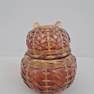May include: A woven wicker basket with a lid, shaped like an owl. The basket is brown and has a natural woven pattern.