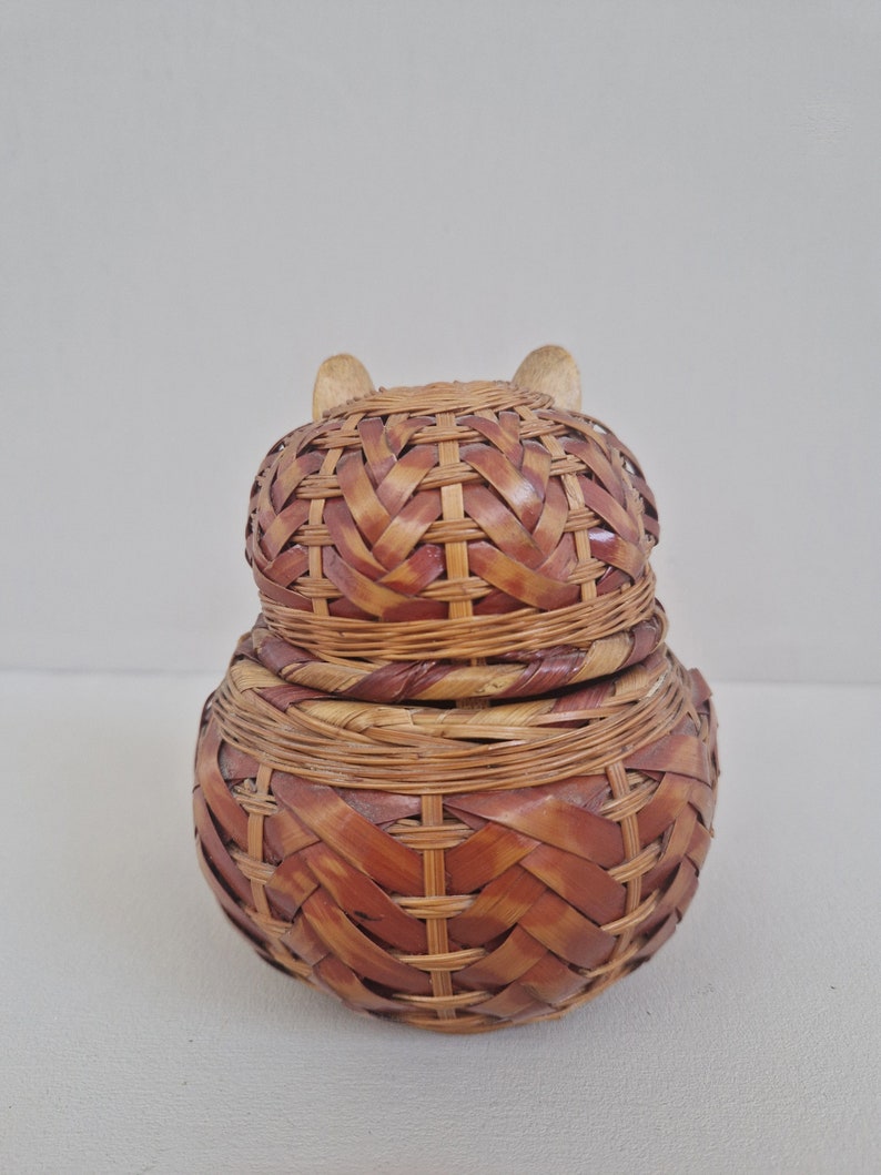 May include: A woven wicker basket with a lid, shaped like an owl. The basket is brown and has a natural woven pattern.