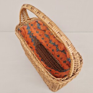 May include: A woven wicker basket with a handle and a floral patterned fabric lining. The basket is empty.