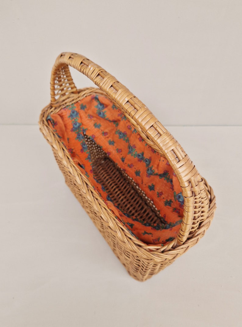May include: A woven wicker basket with a handle and a floral patterned fabric lining. The basket is empty.