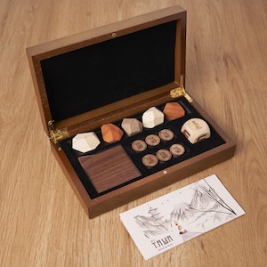 May include: A wooden box with a brown stain and a black velvet interior. The box contains a wooden game with a set of wooden dice, wooden tokens, and a wooden board. The box also includes a set of rules for the game.