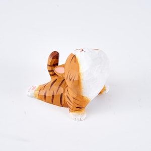 Könnte beinhalten: Holzfigur einer Katze mit orangefarbenen und braunen Streifen, weißen Pfoten und einem weißen Gesicht. Die Katze ist in einer spielerischen Pose dargestellt, mit gebogenem Rücken und erhobenem Schwanz. Handbemaltes, dekoratives Design.