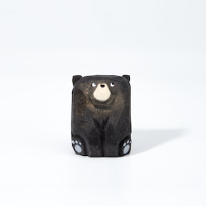May include: A black wooden bear figurine with a white nose and eyes. The bear is sitting with its paws in front of it.