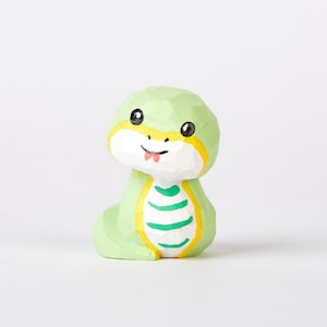 May include: A small, green wooden snake figurine with a yellow belly and green stripes. The snake has a friendly face with black eyes and a red tongue sticking out.