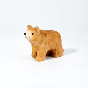 May include: A hand-carved wooden bear figurine with a light brown finish. The bear has a simple, stylized design with a small, black nose and eyes.