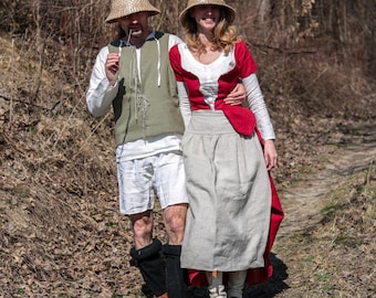 May include: A couple wearing straw hats and medieval-style clothing. The woman is wearing a red and white dress with a long skirt. The man is wearing a green vest and white pants. They are walking on a path in a forest.