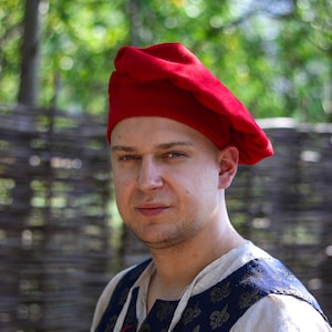 May include: A man wearing a red beret and a blue and gold patterned shirt.