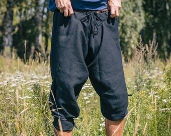 Op de afbeelding: Zwarte broek met een tailleband met trekkoord, een losvallend model met een verlaagd kruis en een kortere lengte die onder de knieën valt. De broek is gemaakt van een effen zwarte stof met een duidelijk zichtbare textuur.