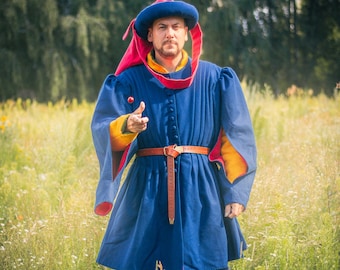 Peut inclure: Une tunique bleue à manches longues avec une doublure jaune et une rangée de boutons sur le devant. Le vêtement comporte une ceinture en cuir marron à la taille et un chapeau bleu assorti avec une longue queue en tissu rouge sur les épaules.