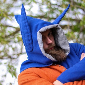 May include: A person wearing a blue hooded garment with large pointed ears. The hood has a gray lining and the garment is made of a soft, fuzzy fabric.