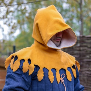 Può includere: Un capo giallo con cappuccio e colletto a festoni. Il cappuccio è tirato sopra la testa e il colletto è visibile intorno al collo.