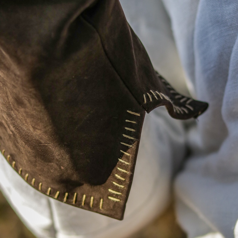 May include: Close-up of a brown suede jacket with a white stitched trim. The jacket is folded and the stitching is visible along the edge.