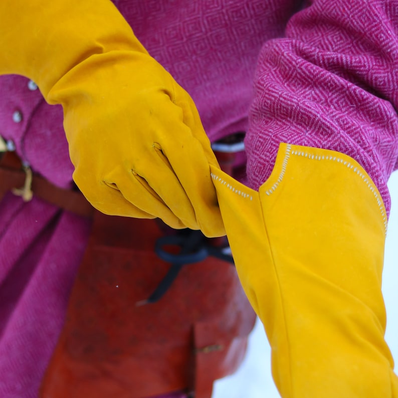 May include: A pair of long yellow leather gloves with a pink and white patterned fabric in the background.