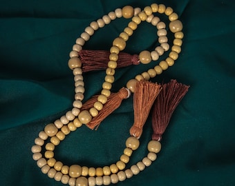 May include: A wooden prayer bead necklace with brown and orange tassels. The beads are a light beige color and are strung together in a circular shape.