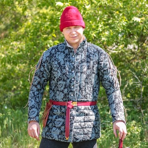 Könnte beinhalten: Ein Mann trägt einen roten Hut und eine blaue und schwarze gesteppte Jacke mit Blumenmuster. Er trägt einen roten Gürtel mit einer goldenen Schnalle.