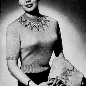 Könnte beinhalten: Nahaufnahme einer Frau, die einen grauen Strickpullover mit geometrischem Muster am Ausschnitt trägt. Der Pullover hat kurze Ärmel und eine figurbetonte Silhouette.