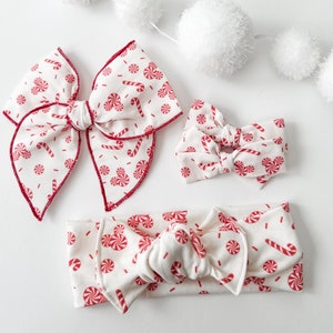 May include: A set of three white headbands with a red and white candy cane and peppermint pattern. The headbands are made of soft, stretchy fabric and are perfect for adding a festive touch to any outfit.