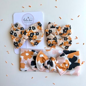 Op de afbeelding: Een set bloemen haaraccessoires, waaronder twee strikclips, een hoofdband en een grotere strikclip. De stof heeft een patroon van zwarte, bruine en witte bloemen. De accessoires worden gepresenteerd op een wit oppervlak met de merknaam "koko bee".