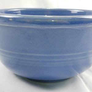 May include: A blue ceramic bowl with a rounded shape. The bowl has a smooth, glossy finish and a slightly flared rim. Horizontal grooves encircle the bowl's exterior, adding a subtle texture. The bowl is suitable for serving food.