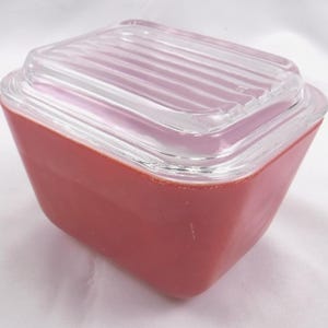 May include: A rectangular storage container with a matte coral-colored base and a clear, ribbed glass lid. The container features tapered sides and a wide opening, with the lid fitting securely into the top rim of the base for a closed unit.