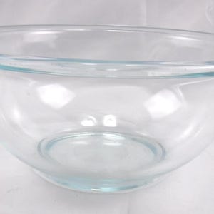 May include: A clear glass mixing bowl with a smooth, rounded interior and a wide, flat rim. The bowl features a transparent design with a subtle blue-tinted hue, showcasing a deep, circular basin and a sturdy base for stability during food preparation.