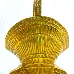 May include: A gold-colored, decorative basket with a handle. The basket has a shell-like design with vertical and horizontal lines. The handle is braided. The basket is made of metal and is likely used for decorative purposes.
