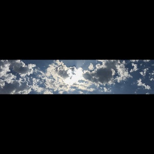 May include: A bright blue sky with fluffy white clouds and the sun shining through.