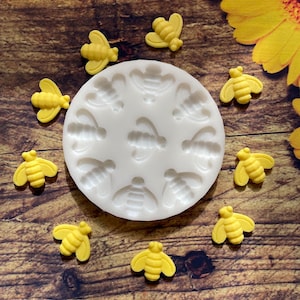 May include: A white silicone mold with 10 bee-shaped cavities. The mold is surrounded by 10 yellow bee-shaped candies.