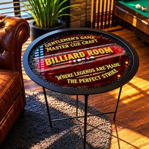 Peut inclure: Une table d'appoint ronde en métal noir avec un plateau décoratif. La surface de la table présente les mots "BILLIARD ROOM" en lettres dorées, sur un fond rouge et marron avec des boules de billard. Le texte "GENTLEMEN'S GAME MASTER CUE CRAFT" et "WHERE LEGENDS ARE MADE THE PERFECT STRIKE" sont également visibles.